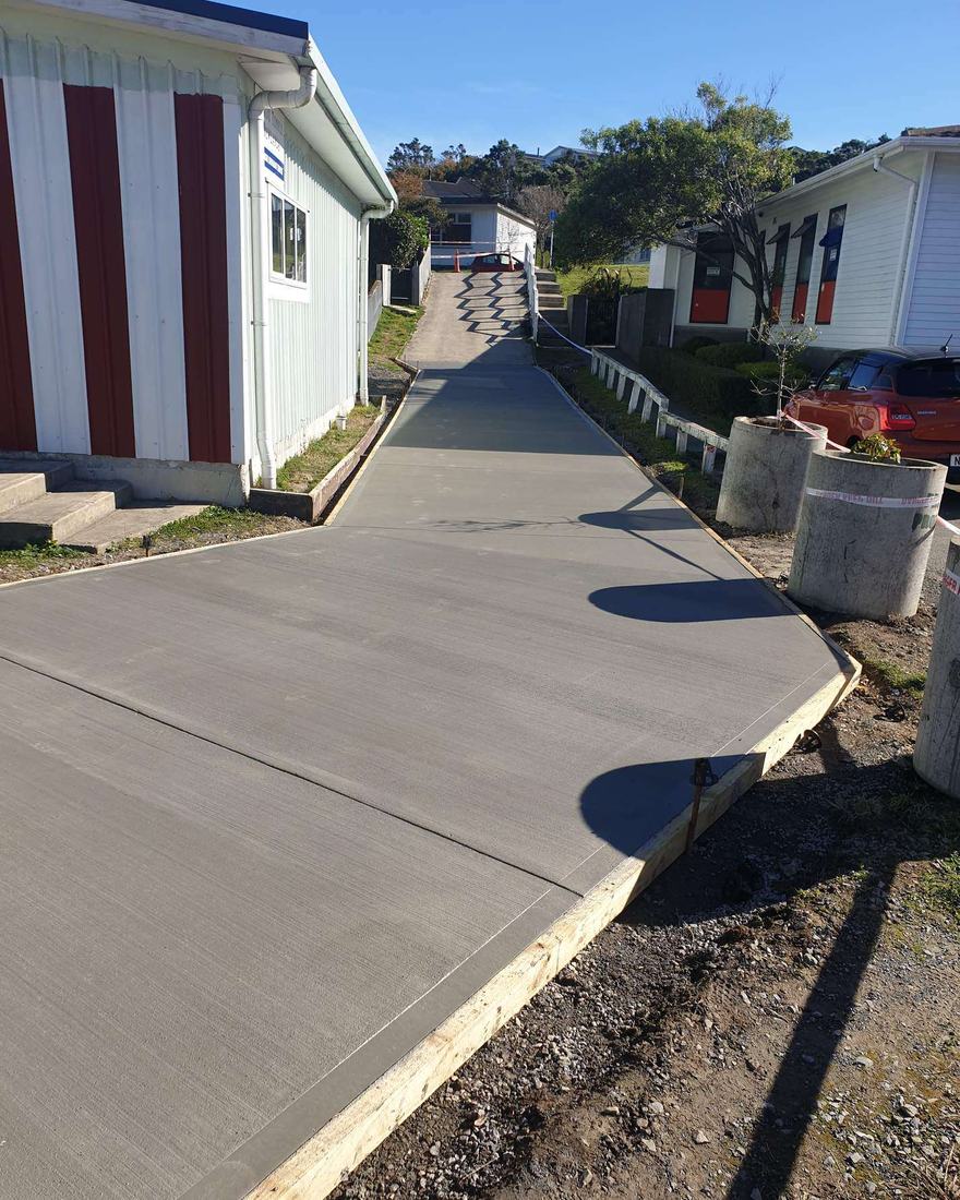 New concrete path curving up a slope beside a red and white building