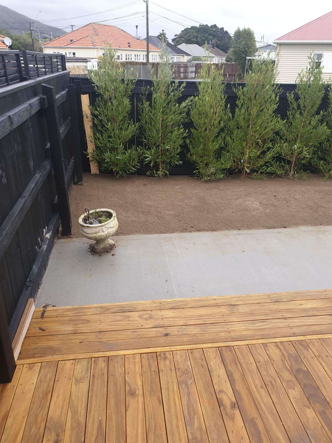 New timber deck and concrete patio with a levelled bed along a black fence