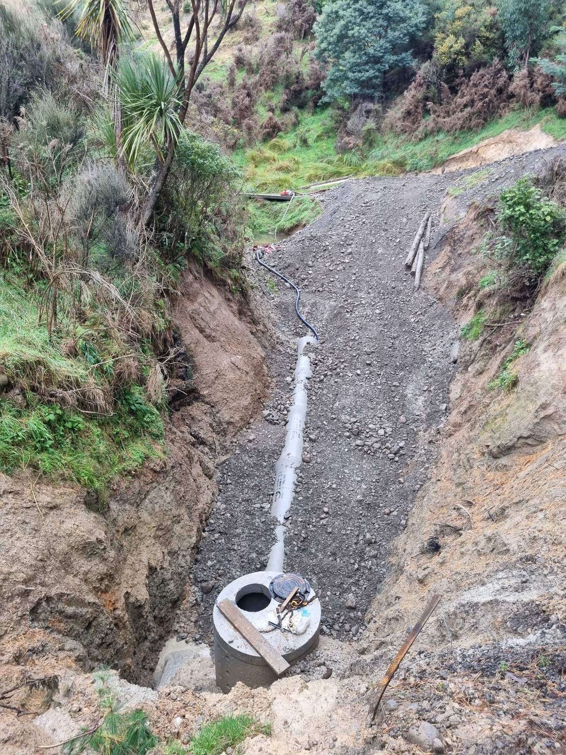 Drainage pipe bedded in gravel down a cut gully to a concrete manhole