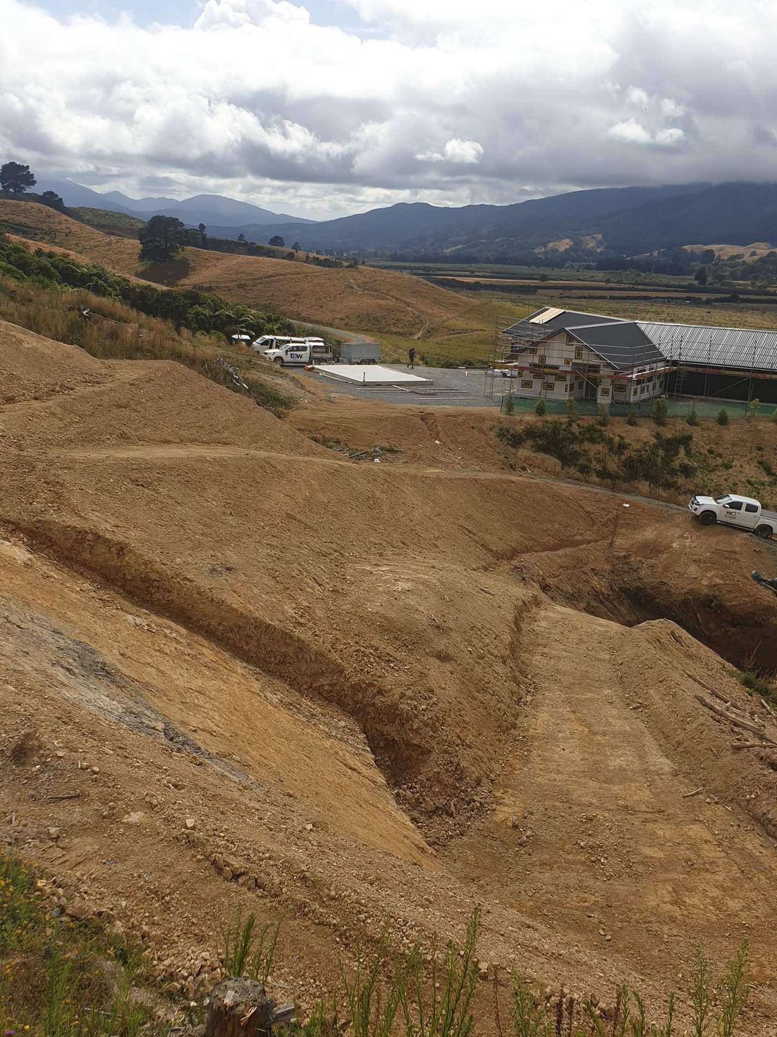 Benched earthworks cuts on a hillside looking down to houses in the valley