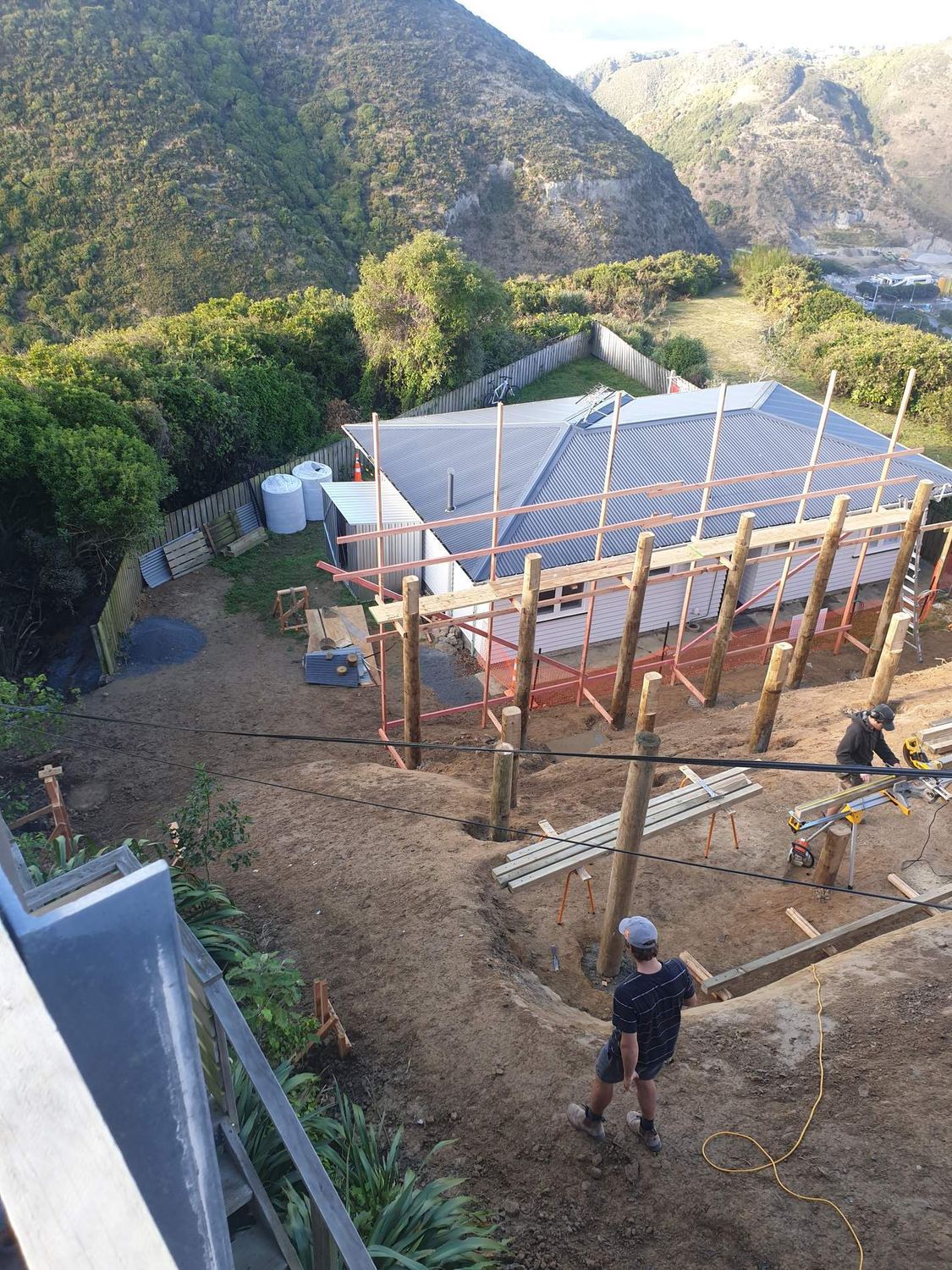 Timber pole foundations set out for a house on a steep site, with the crew at work