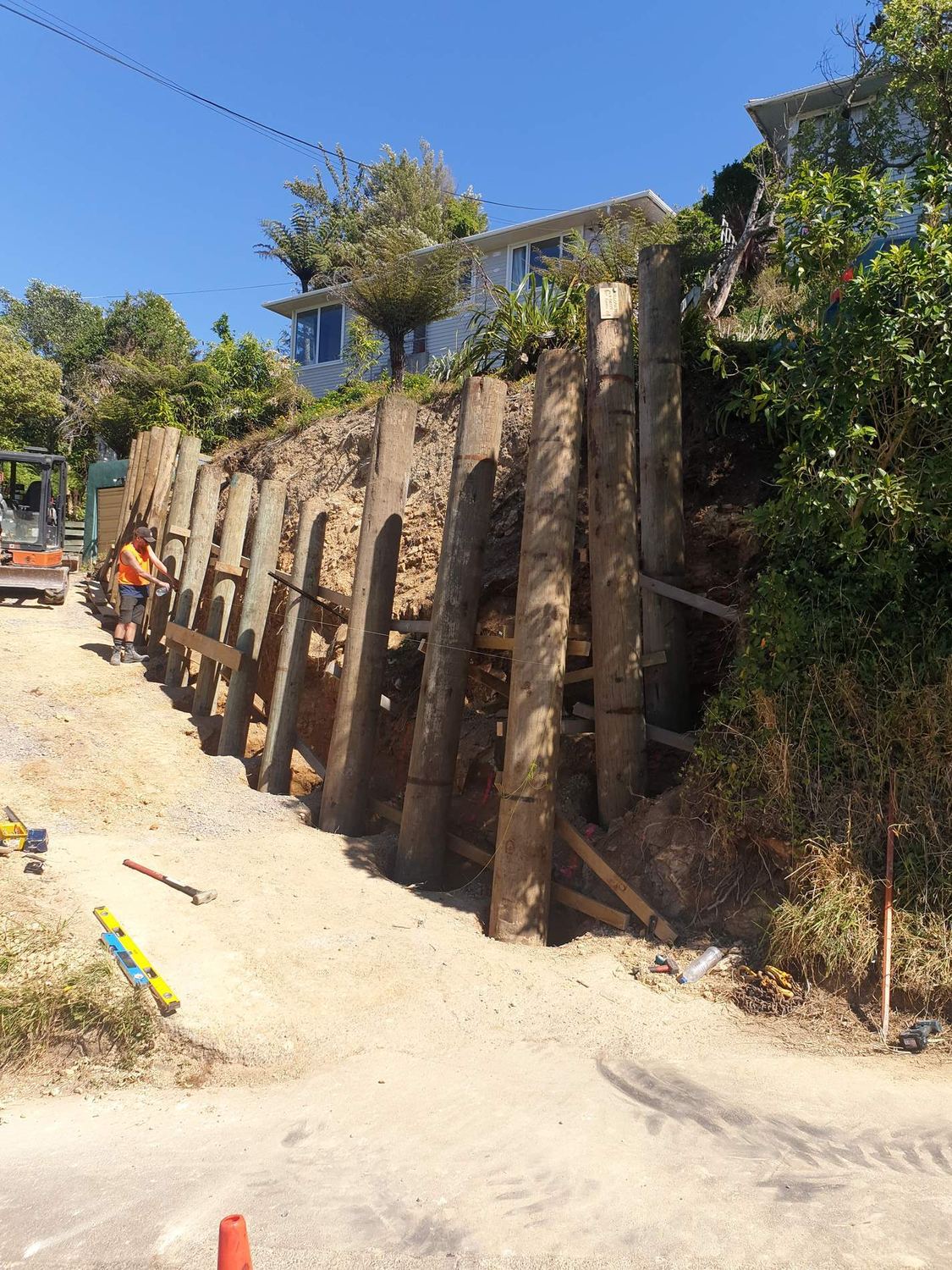 Tall timber pole retaining wall along a steep bank below a house