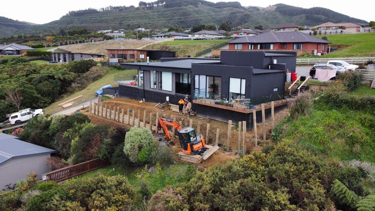 Elevated view of a mini excavator and crew building a pole wall in front of a modern house