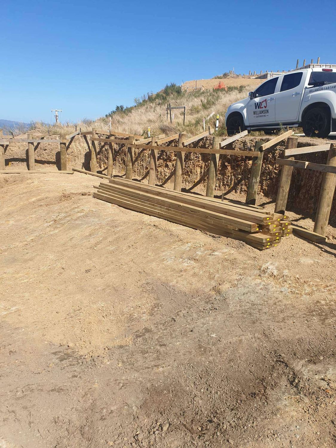 Post and rail timber barrier on a dry hilltop site with timber stacked on the ground