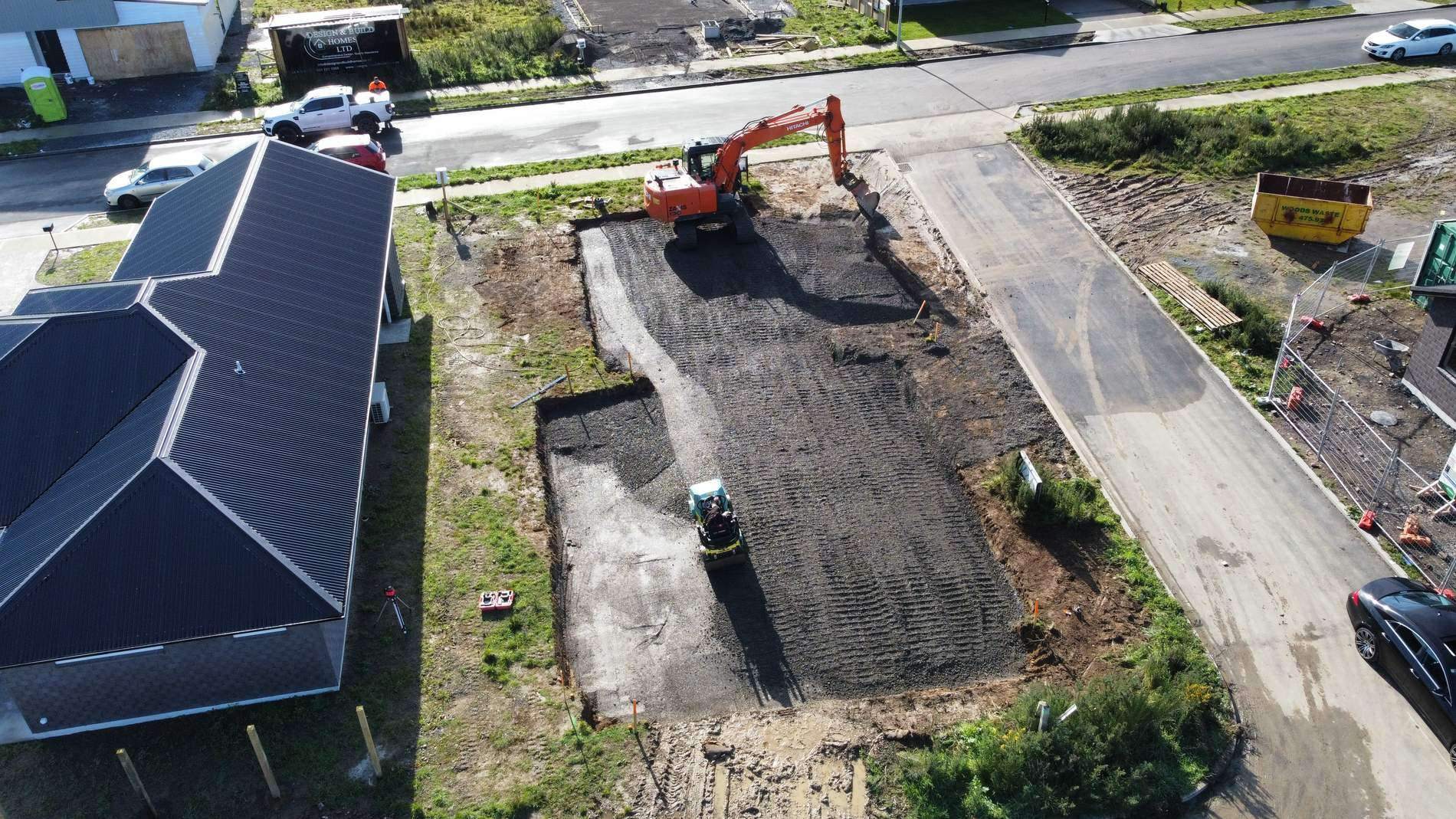 Aerial view of an excavator and roller forming a driveway beside a new house in a subdivision