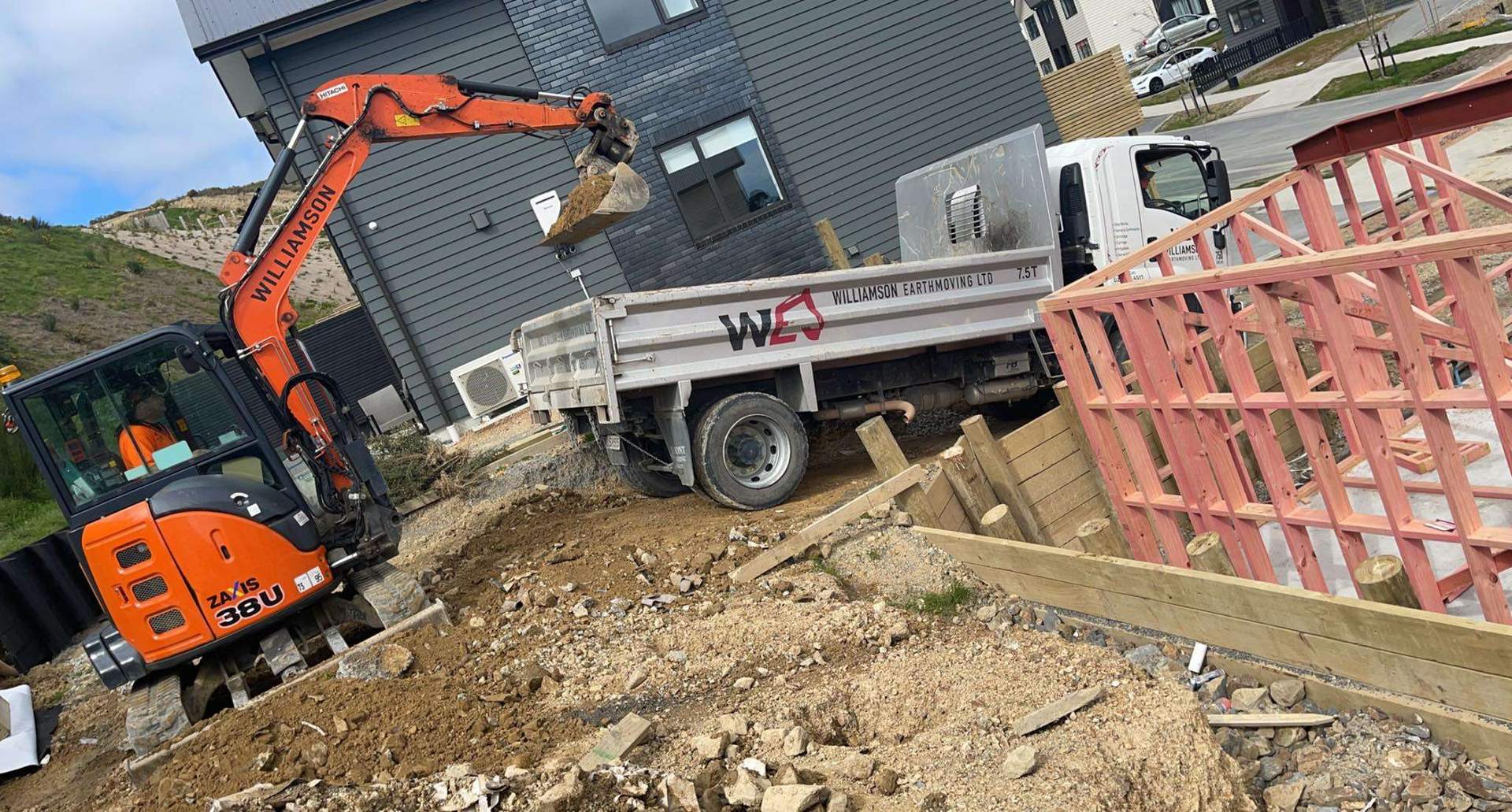 Williamson Earthmoving mini excavator loading the company tipper truck beside a new two-storey house